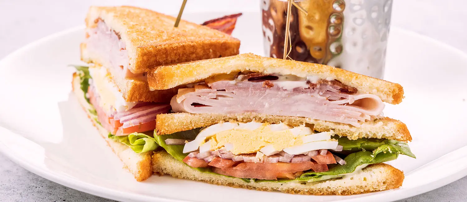 Clubhouse sandwich layered with bacon, turkey, egg, tomato, and lettuce