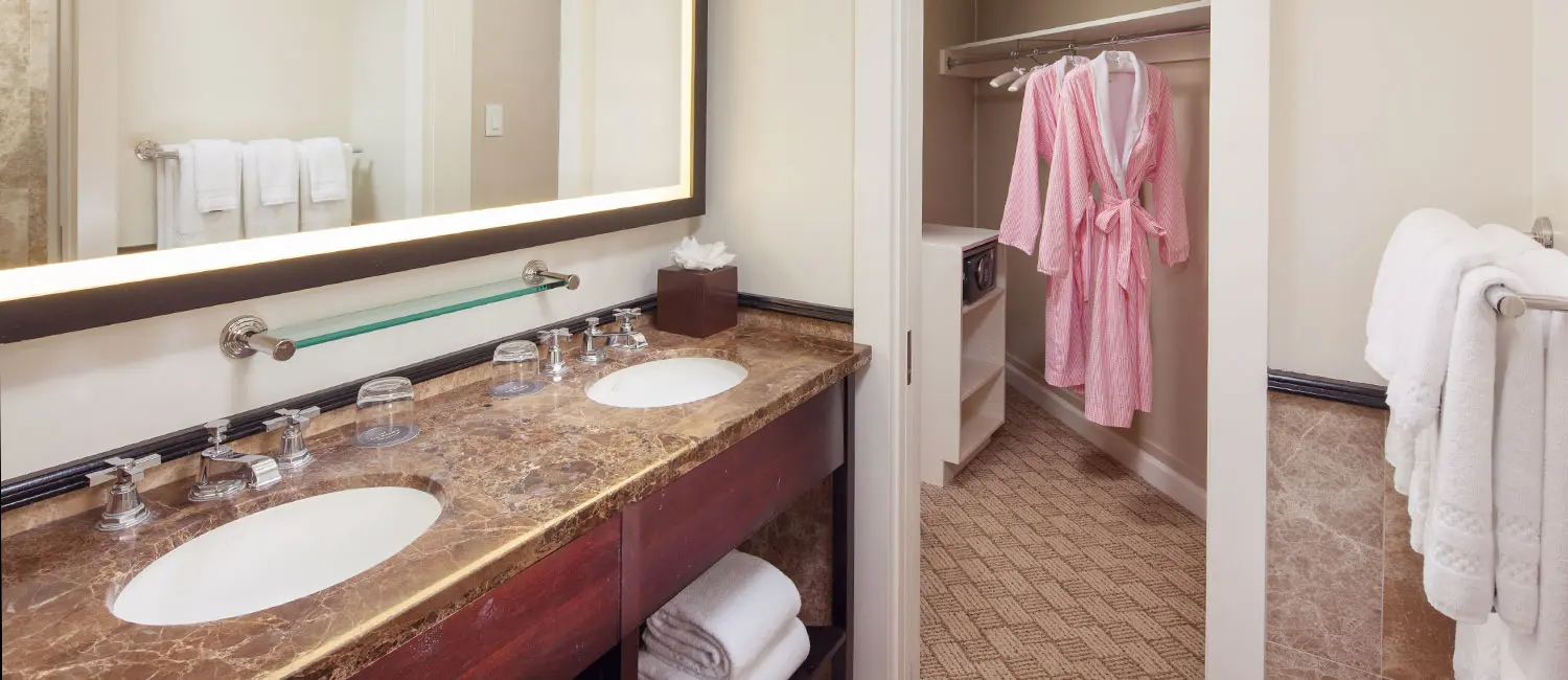 Bathroom with double sinks and adjoining closet with robes.