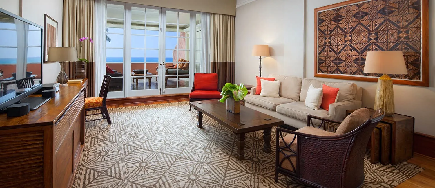 Living room of the Kamehameha Suite with an ocean view beyond the windows.